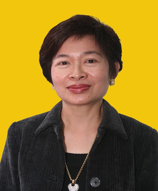 Smiling woman in charcoal jacket with gold necklace on yellow background, conveying professionalism.