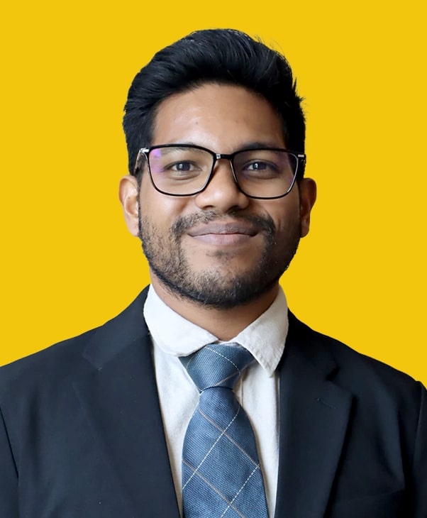 Smiling man in suit and tie with glasses against yellow background, exuding confidence and warmth.