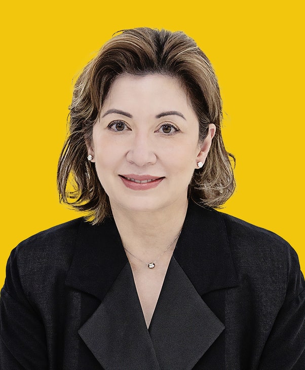 Woman with brown hair in black suit, smiling against yellow background.