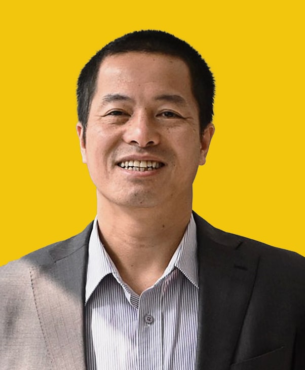 Man in suit with striped shirt, smiling against yellow background.