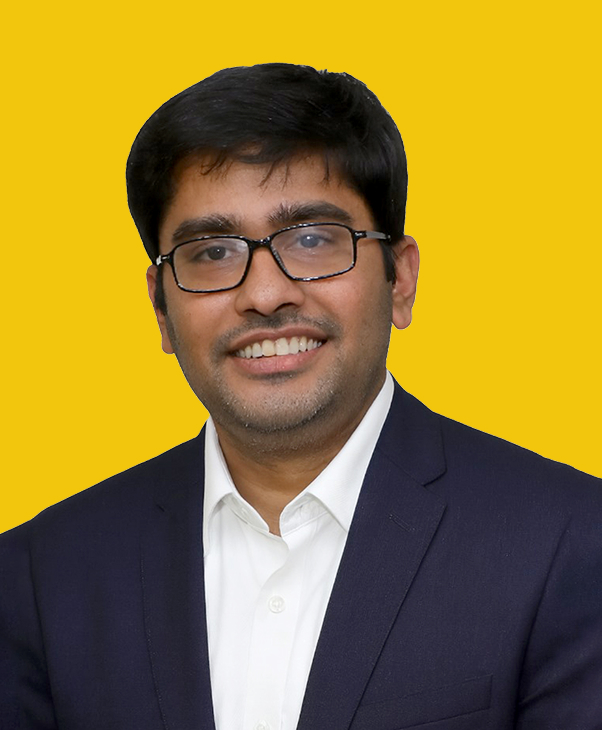 Smiling man in glasses, navy suit, white shirt on yellow background.