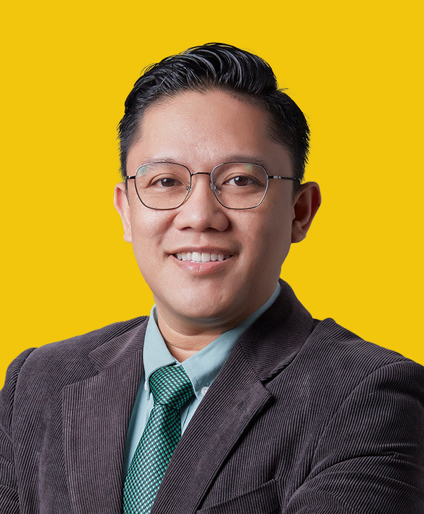 Person with glasses, brown blazer, green tie on yellow background.