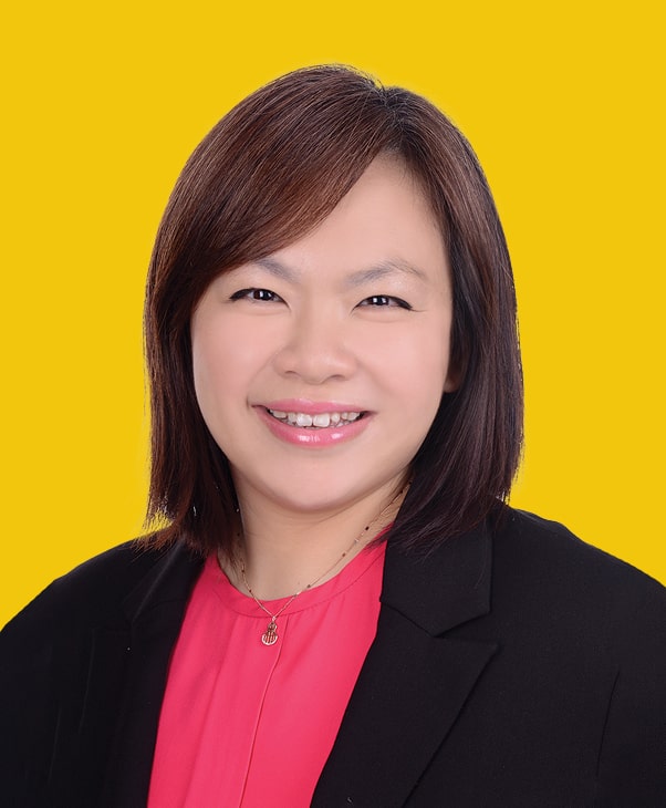 Smiling person in black blazer and pink shirt on yellow background, radiating confidence.