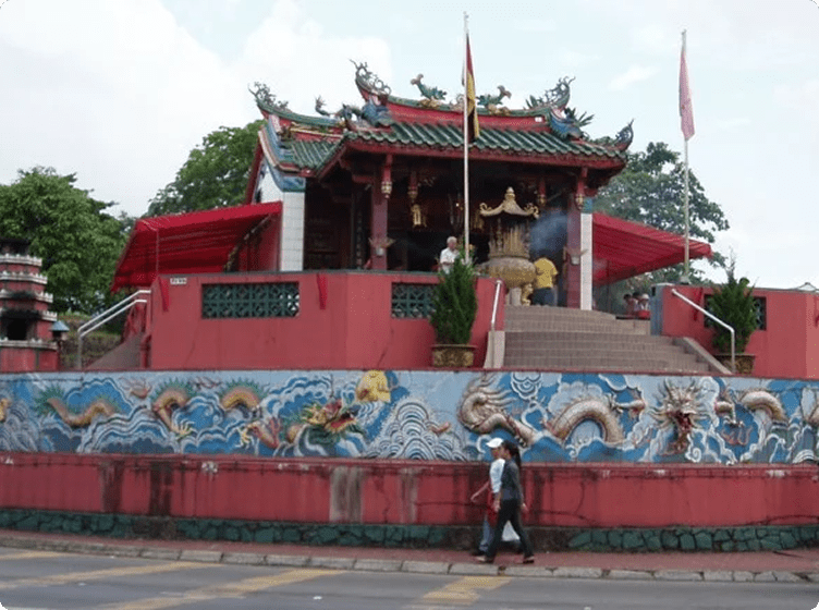 Chinese temple with ornate roof, dragon mural, and rising incense smoke; two people walk by.