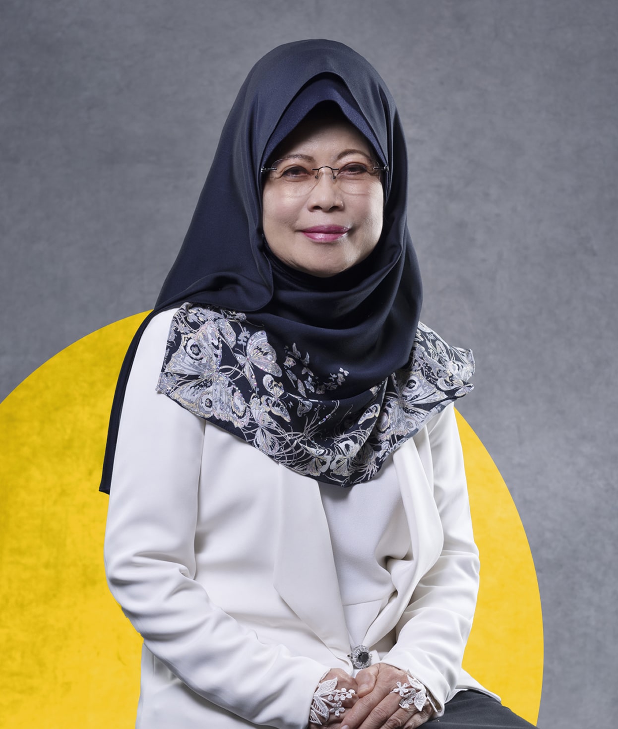 Woman in hijab and white blazer smiles confidently against a gray background with a yellow semi-circle.