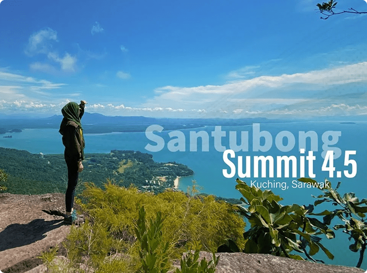 Person on rocky cliff views green landscape and blue water under clear sky; text: "Santubong Summit 4.5, Kuching, Sarawak."