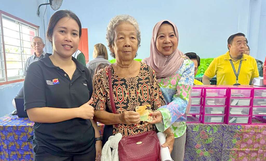 Three women stand together as an elderly woman holds a card, all smiling warmly.