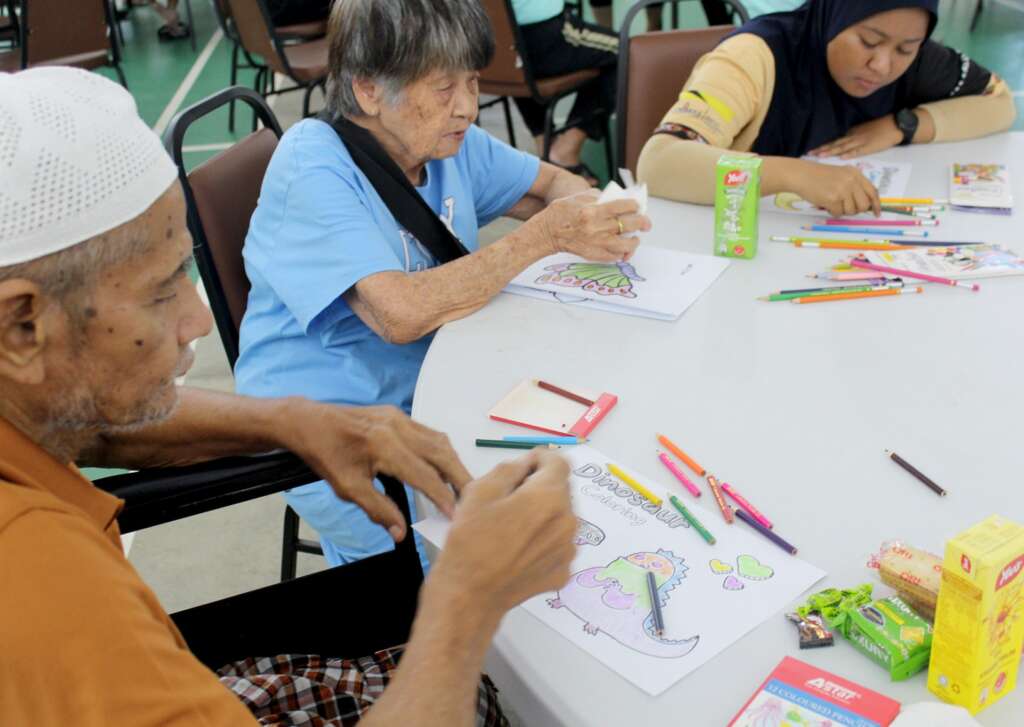 A diverse group sits around a table, calmly coloring with crayons and pencils.